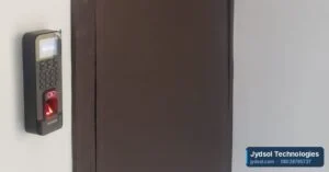 Biometric fingerprint reader mounted on the wall beside an office door