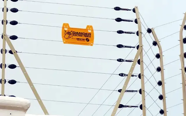 Electric fence wires, insulators and warning sign on a perimeter wall